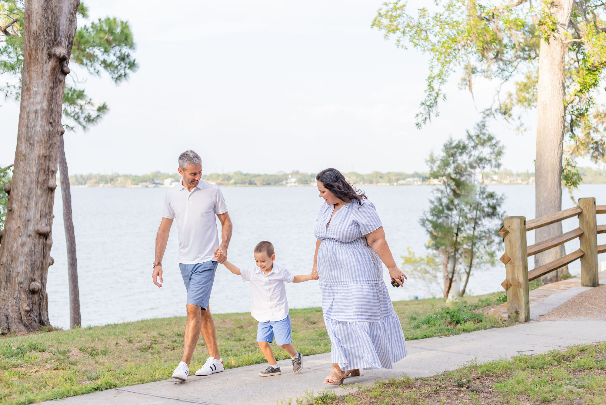 A family of four holding hands and smiling in a park with an ocean view in the background.