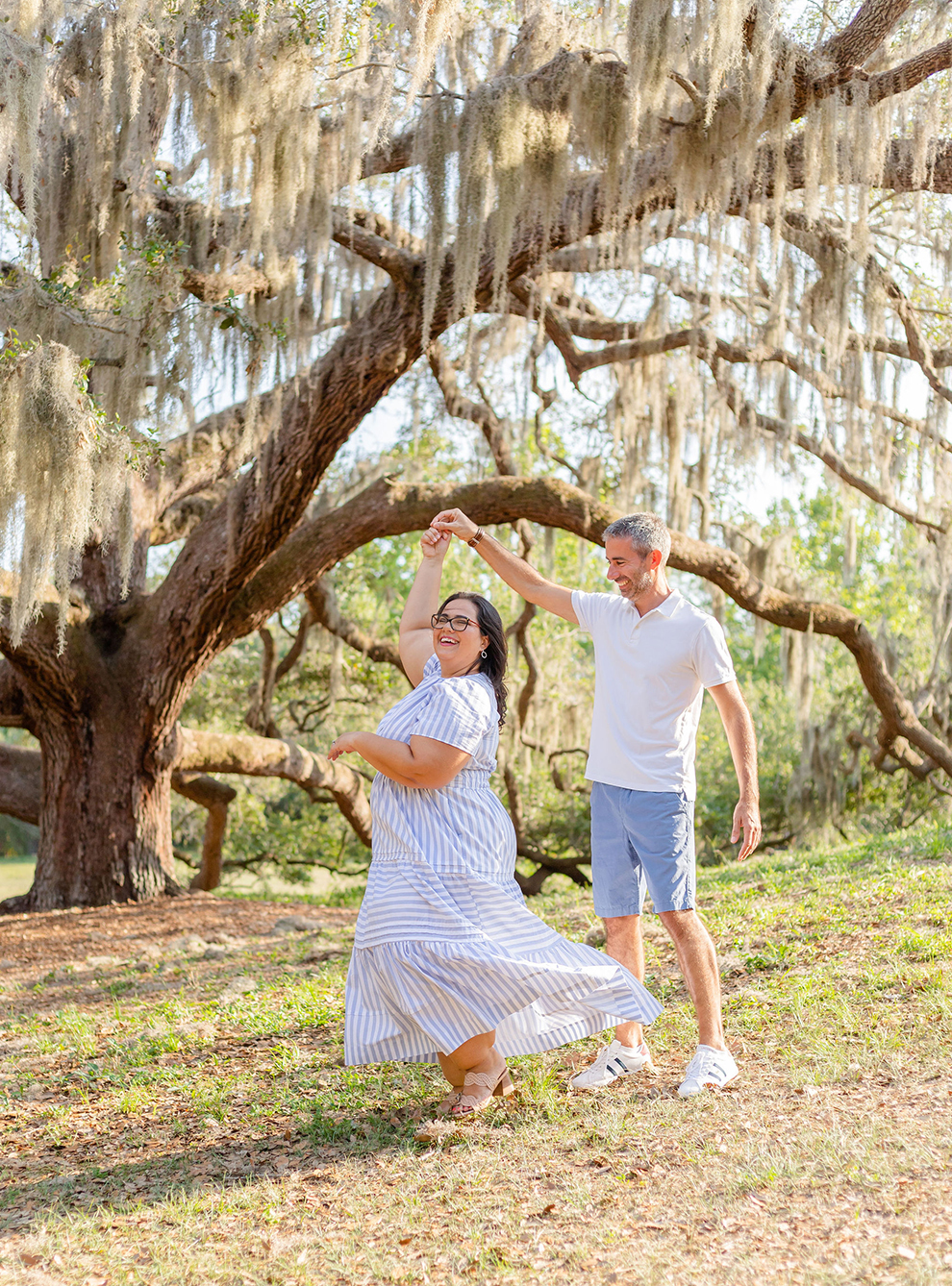 Husband twirling dancing with his wife at a park, Spanish moss