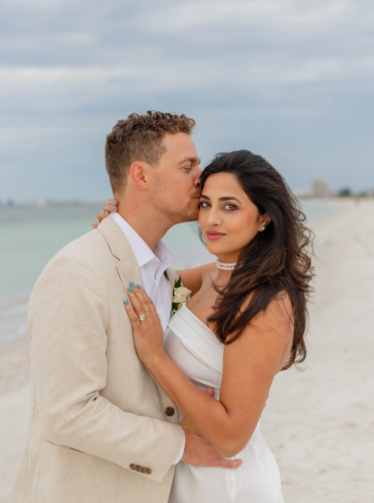 The groom gives bride a soft kiss on the forehead at the beach wedding 