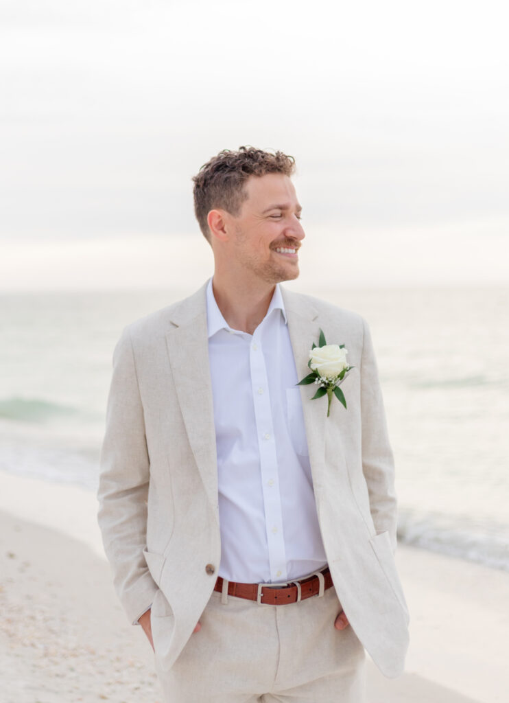 Groom Zach in a beige suit posing on the sandy shore of Saint Pete Beach.