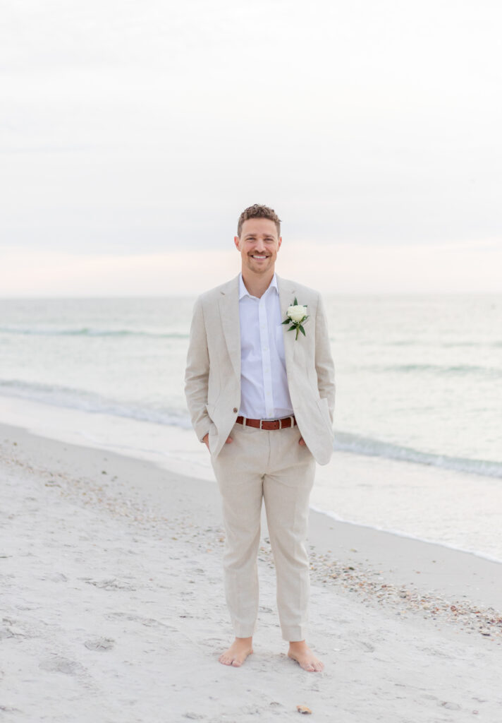 Groom Zach in a beige suit posing on the sandy shore of Saint Pete Beach.