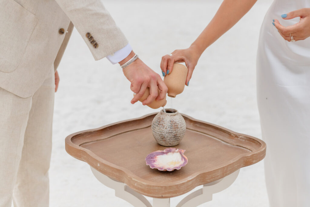 Creating a Keepsake: "Siddhi and Zach pouring beach sand in a keepsake container during their intimate Saint Pete Beach wedding ceremony.