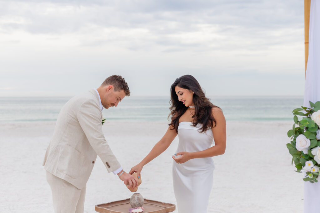 Creating a Keepsake: Siddhi and Zach collect beach sand in a keepsake container during their intimate Saint Pete Beach wedding ceremony.