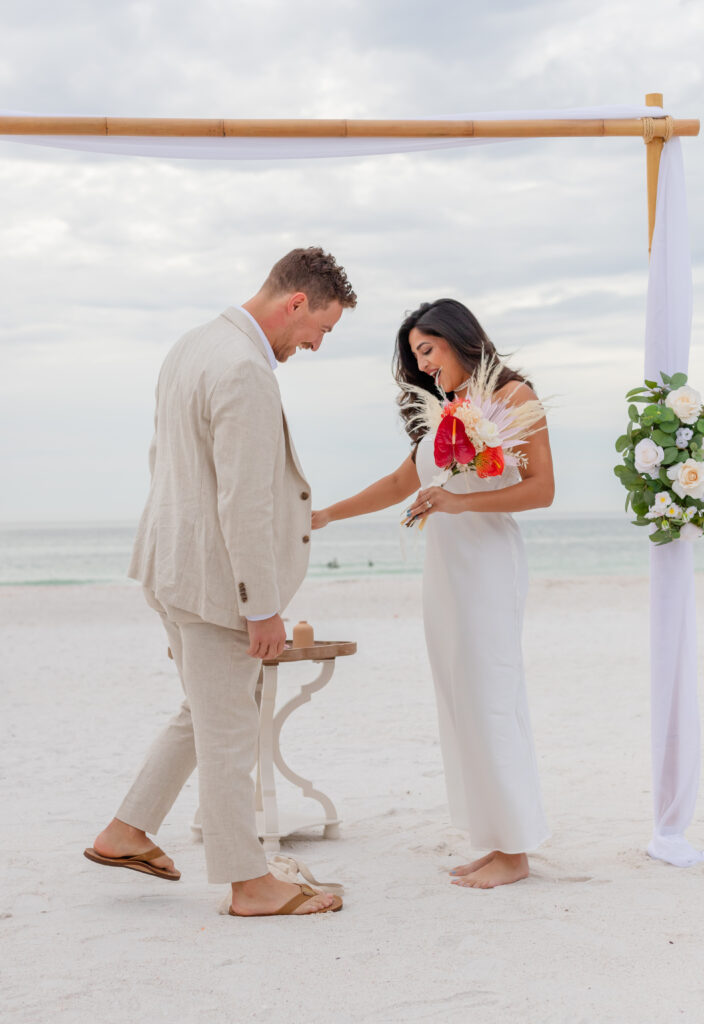 Siddhi and Zach performing the tradition of breaking the glass during their beach wedding ceremony