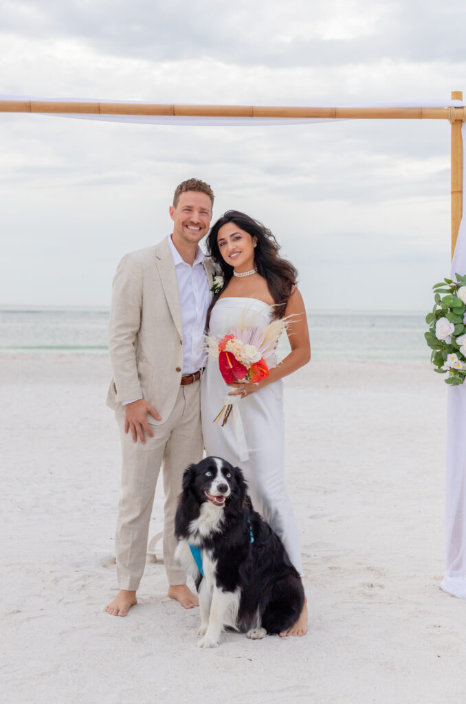 Wedding couple posing with their dog on the beach in Saint Pete, showcasing their love and joy on their wedding day.